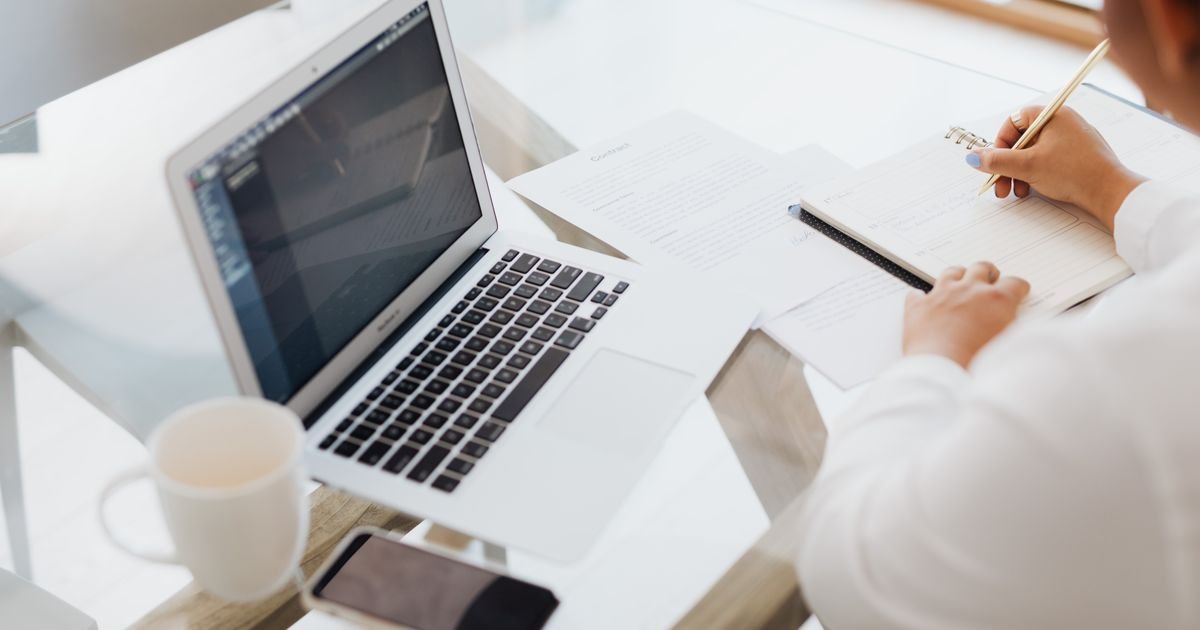 Laptop, notebook and coffee cup arranged on a glass desk