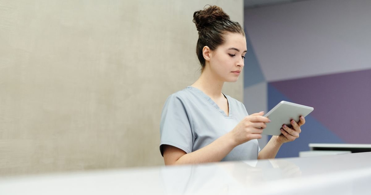 Receptionist in scrubs using a tablet at a clinic reception desk