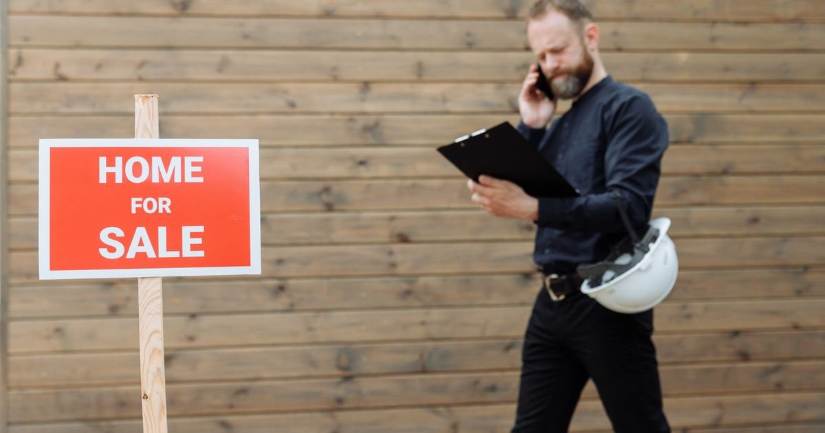 Real estate agent taking a call outside a property with a home for sale sign